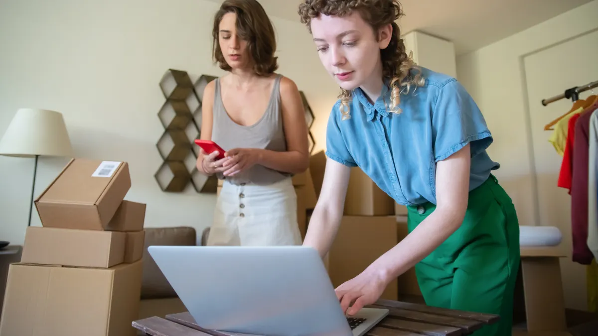 two women packing products at a laptop with boxes